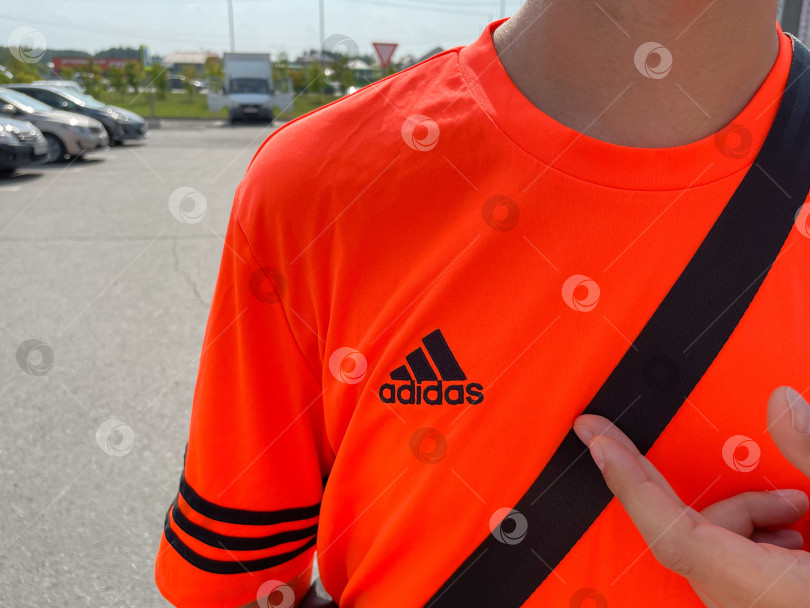 Скачать Тюмень, Россия - 30 августа 2022 года: логотип Adidas на оранжевой футболке. Adidas - немецкая транснациональная корпорация по производству одежды и обуви фотосток Ozero