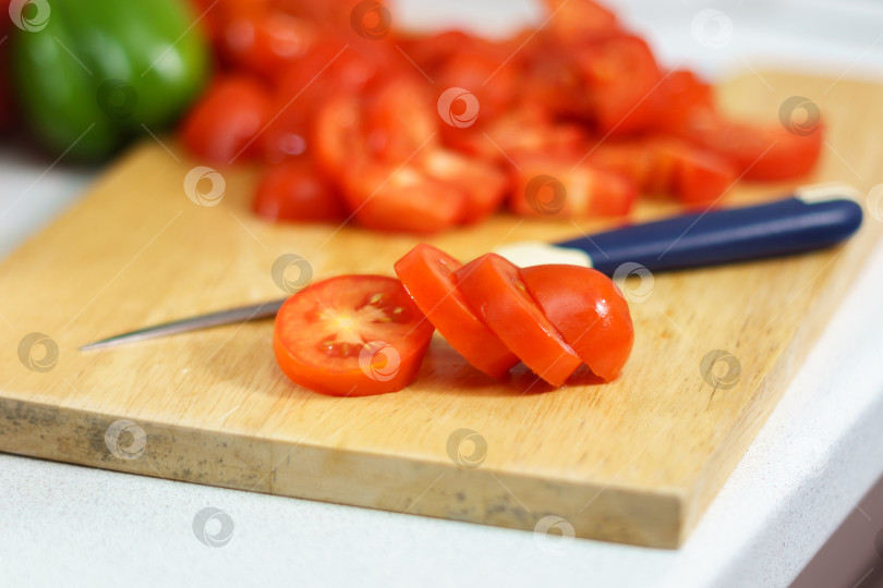 Скачать Сочные красные помидоры нарезают ломтиками на деревянной разделочной доске. Приготовление овощей, вегетарианской пищи фотосток Ozero