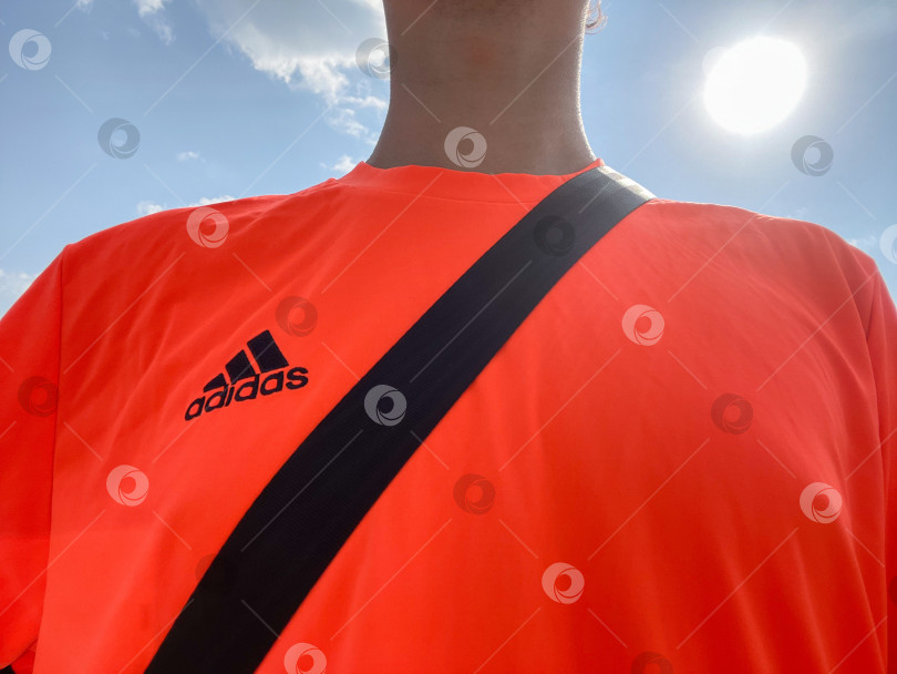 Скачать Тюмень, Россия - 30 августа 2022 года: логотип Adidas на оранжевой футболке. Adidas - немецкая транснациональная корпорация по производству одежды и обуви фотосток Ozero