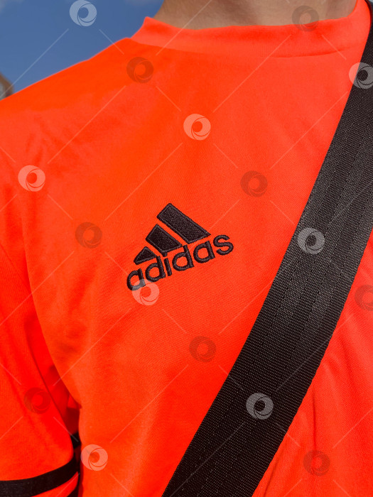 Скачать Тюмень, Россия - 30 августа 2022 года: логотип Adidas на оранжевой футболке. Adidas - немецкая транснациональная корпорация по производству одежды и обуви. Вертикальная фотография фотосток Ozero