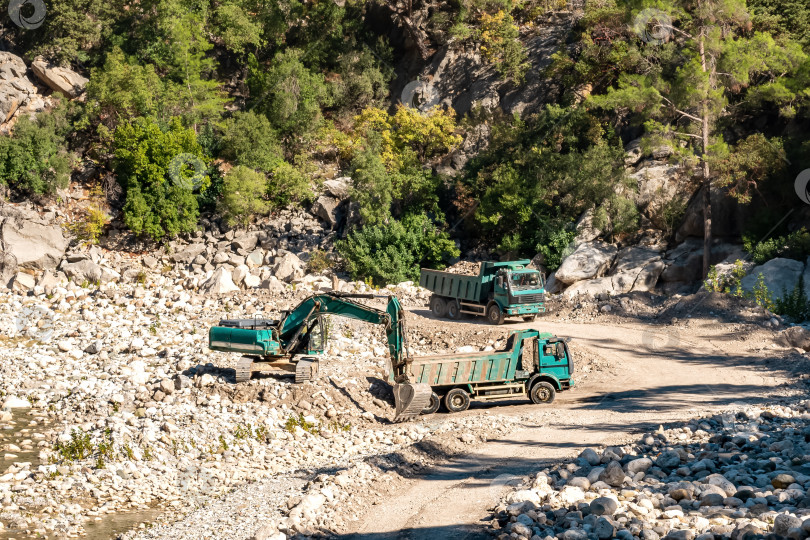 Скачать дорожные работы в долине реки, экскаваторы и самосвалы перемещают камни фотосток Ozero