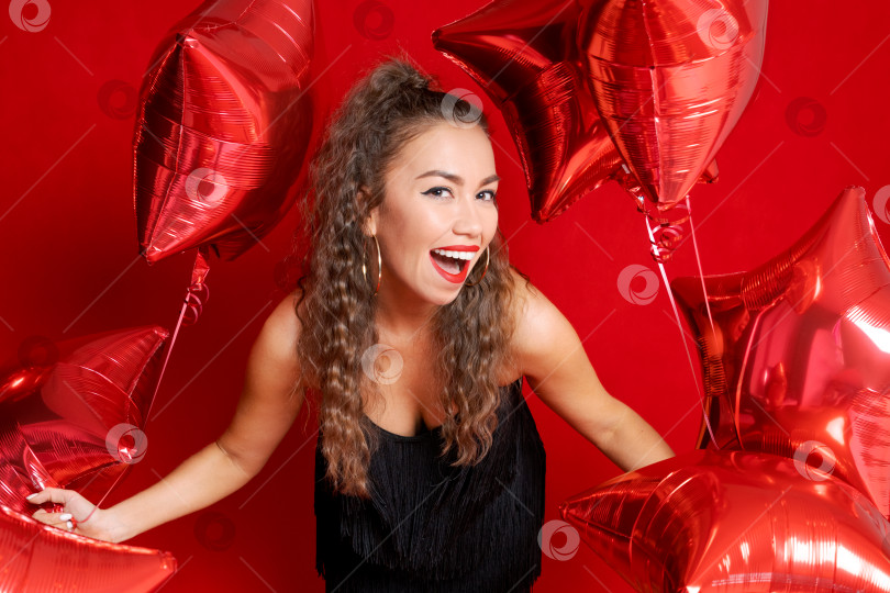 Скачать Красивая молодая радостная девушка держит в руках связку воздушных шаров с красными звездами на красном фотосток Ozero