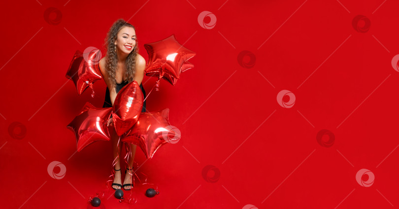Скачать Улыбающаяся счастливая кавказская девушка в черном платье с красными воздушными шарами в форме звезд фотосток Ozero