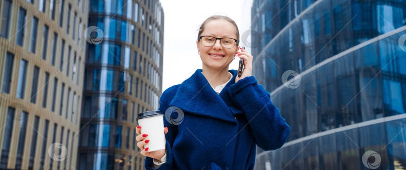 Скачать Деловая женщина с телефоном возле офиса. Портрет улыбающейся девушки в синем пальто фотосток Ozero