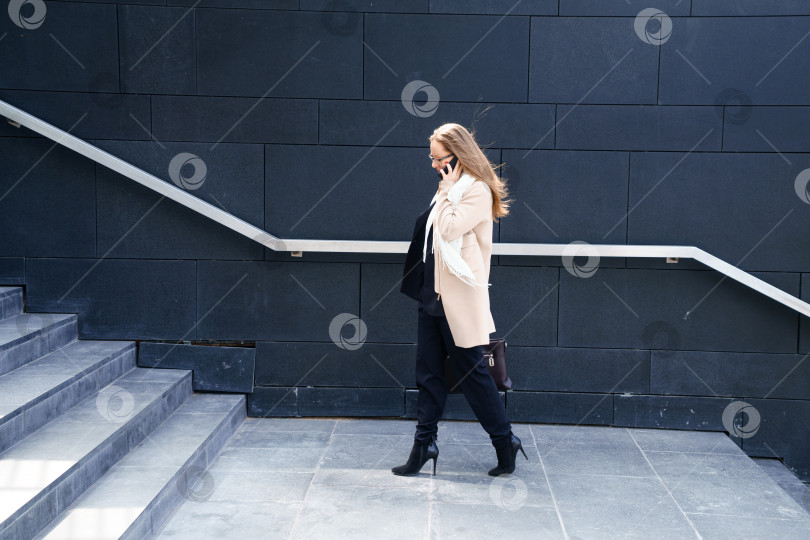 Скачать Деловая женщина в пальто с сумкой в руках поднимается по ступенькам к зданию фотосток Ozero