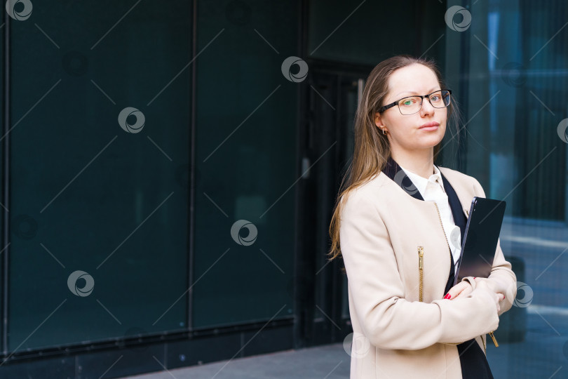 Скачать Деловая женщина с папкой в руке и в очках возле бизнес-центра фотосток Ozero