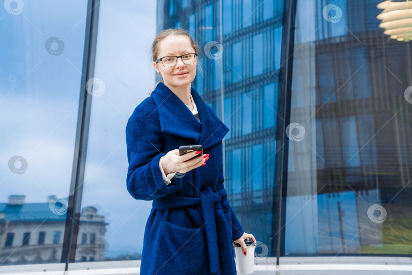 Скачать Успешная женщина в деловой одежде в синем пальто идет по улице возле офиса фотосток Ozero