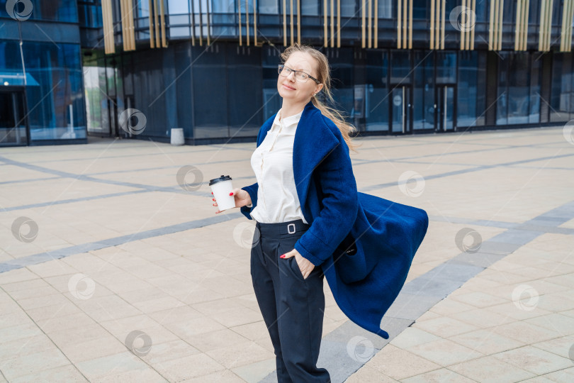 Скачать Успешная женщина в деловой одежде в синем пальто идет по улице возле офиса фотосток Ozero
