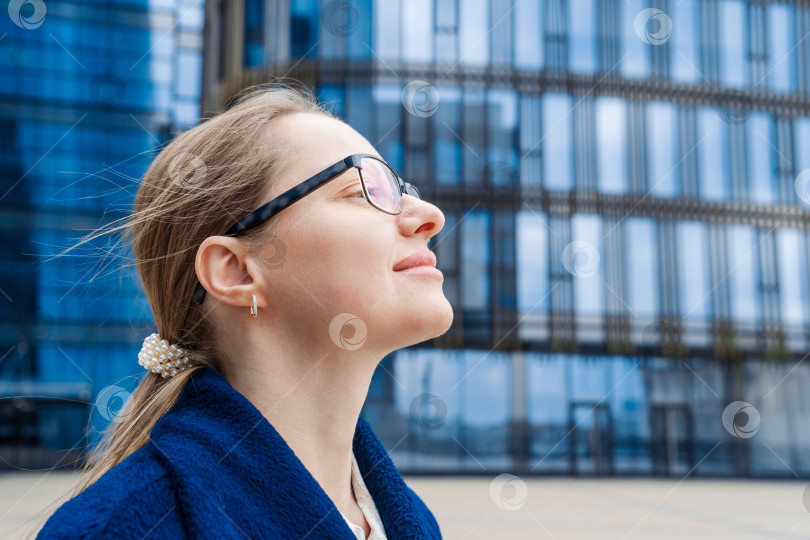 Скачать Портрет счастливой женщины в очках крупным планом, задумчиво смотрящей в сторону, в голубых тонах фотосток Ozero