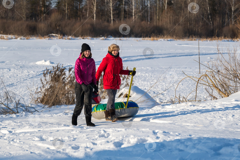 Скачать Две молодые женщины с зимним занятием на сноутюбинге, бегают зимой. Зимние развлечения фотосток Ozero