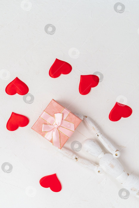 Скачать Розовая подарочная коробка на белом фоне с деревянным манекеном с красными сердечками. Вид сверху. Вертикальная фотография фотосток Ozero