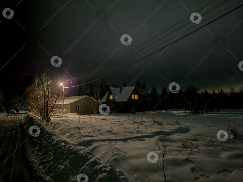 Скачать Русская деревня ночью зимой. Дорога, покрытая снегом, и свет из окон домов фотосток Ozero