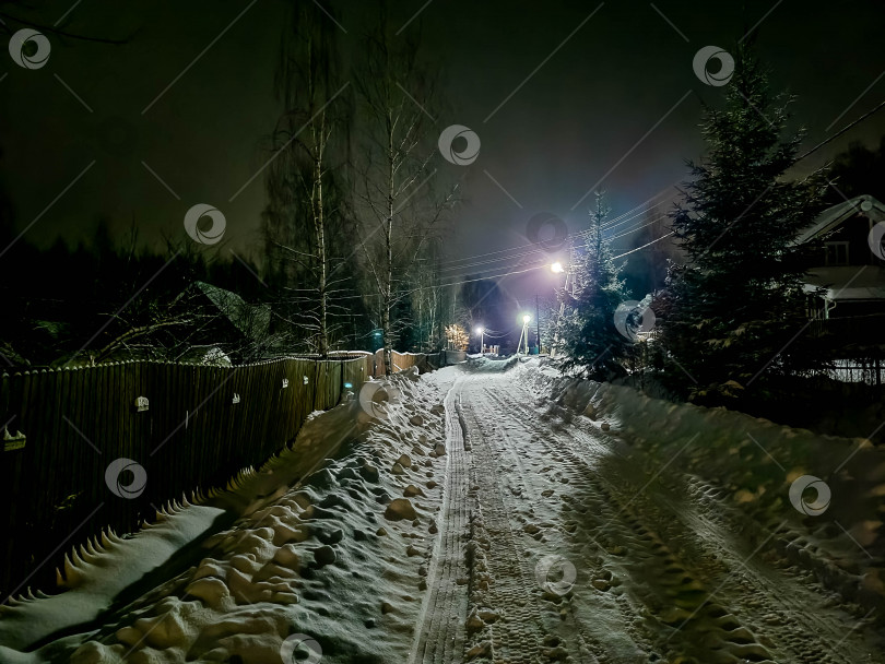 Скачать Русская деревня ночью зимой. Дорога, покрытая снегом, и свет из окон домов фотосток Ozero