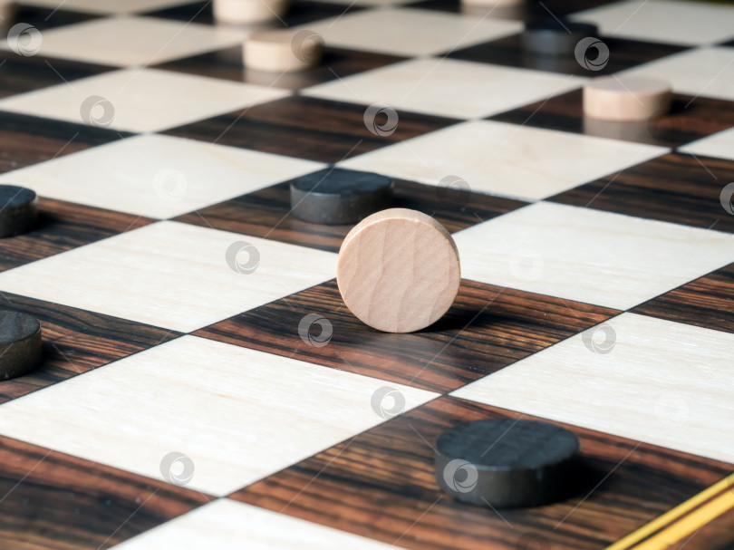Скачать Белая шашка, стоящая на боку в окружении черных шашек на шахматной доске. Избирательный фокус фотосток Ozero