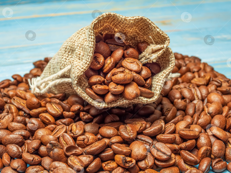 Скачать Открытый джутовый мешочек с кофейными зернами на кучке кофейных зерен. Крупный план. фотосток Ozero
