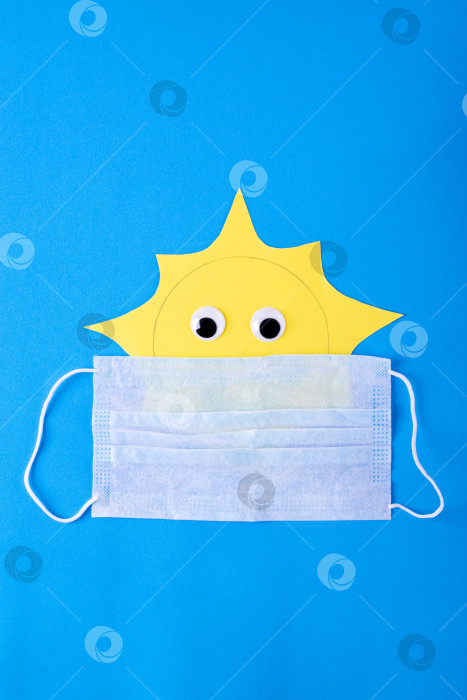 Скачать Бумажное солнце в одноразовой медицинской маске синего цвета. Летние каникулы и ограничения, связанные с covid. фотосток Ozero