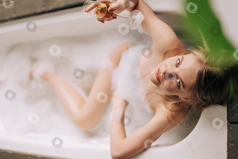 Скачать Вид сбоку красивая молодая женщина пьет шампанское и смотрит в камеру, наслаждаясь ванной с пеной фотосток Ozero