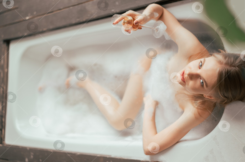 Скачать Вид сбоку красивая молодая женщина пьет шампанское и смотрит в камеру, наслаждаясь ванной с пеной фотосток Ozero