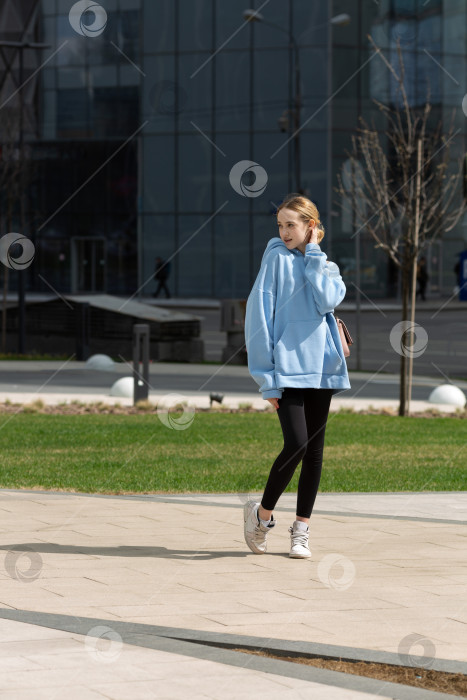 Скачать Девочка-подросток в толстовке с капюшоном и леггинсах гуляет по городу фотосток Ozero