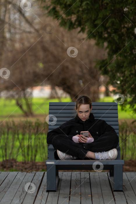 Скачать Девочка-подросток сидит на скамейке с телефоном в руках фотосток Ozero