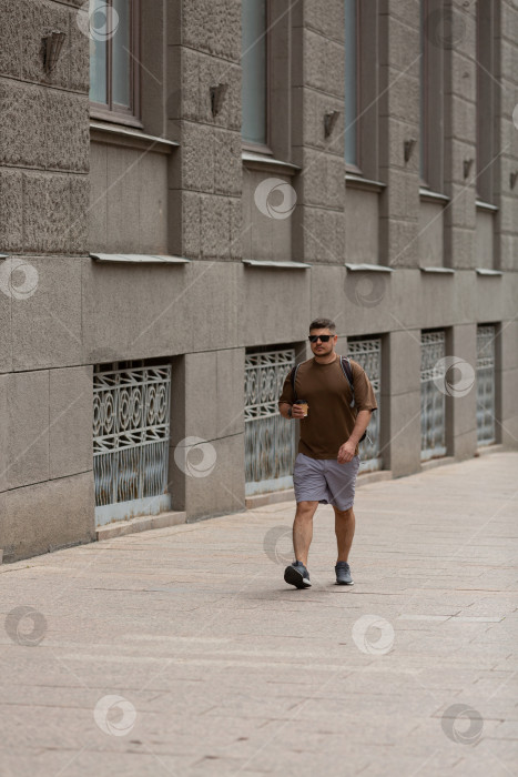 Скачать Мужчина среднего возраста идет по улице с одноразовым стаканчиком кофе фотосток Ozero