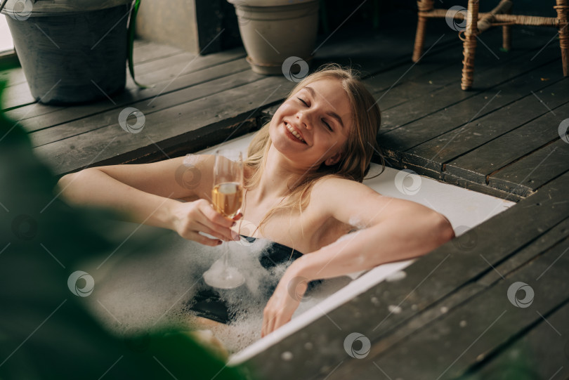 Скачать Красивая молодая женщина пьет шампанское и смотрит в камеру, наслаждаясь ванной с пеной фотосток Ozero