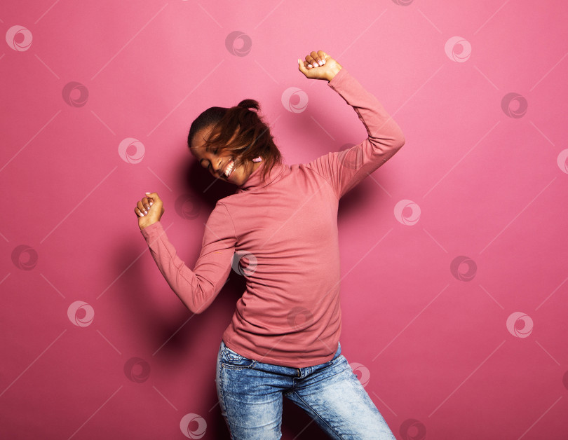 Скачать молодая афроамериканка носит повседневную одежду, танцует, глядя на пустое пространство, изолированное розовым цветом фона фотосток Ozero
