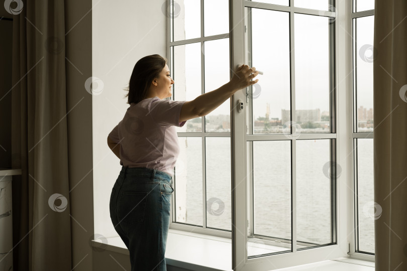 Скачать женщина открывает окно ранним утром, наслаждаясь свежим воздухом фотосток Ozero