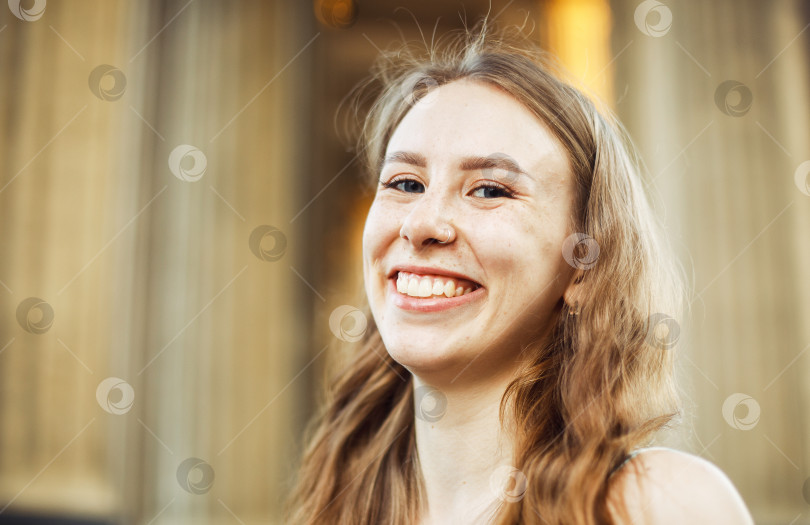 Скачать Крупным планом веселая белокурая молодая женщина на улице, смотрящая в камеру с зубастой улыбкой. фотосток Ozero