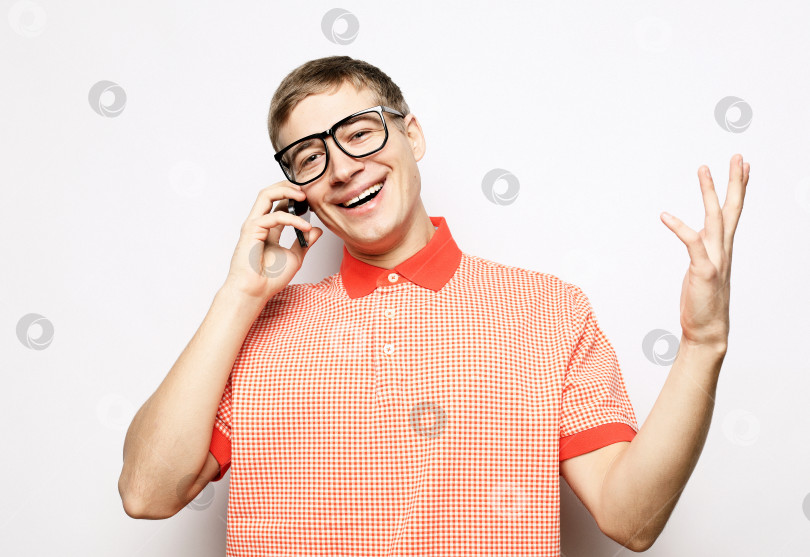 Скачать Счастливый молодой человек в рубашке жестикулирует и улыбается, разговаривая по мобильному телефону фотосток Ozero