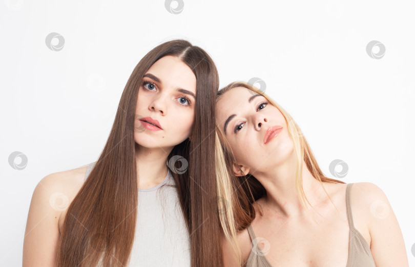 Скачать Две молодые женщины с длинными волосами стоят вместе на белом фоне, позируют, смотрят в камеру фотосток Ozero