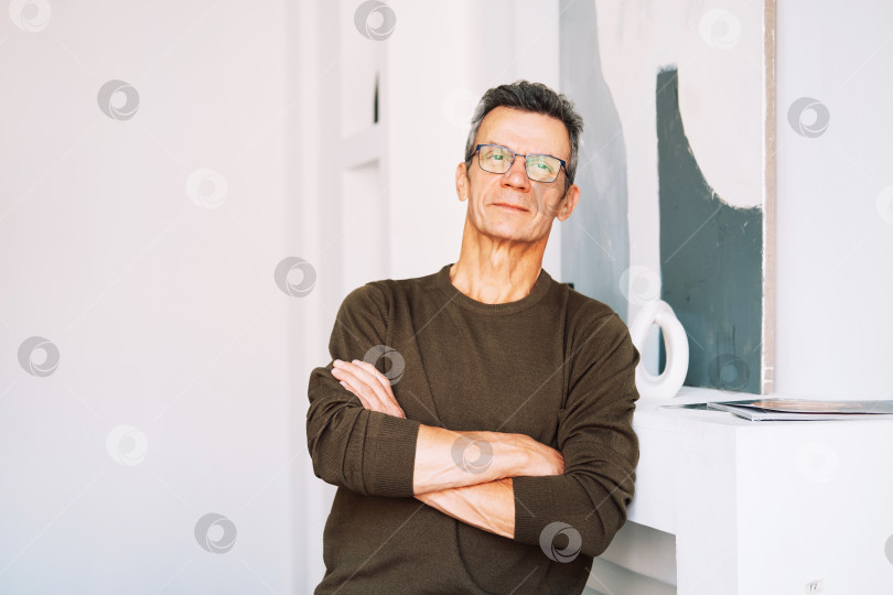 Скачать Красивый одинокий мужчина средних лет 60-х годов смотрит в камеру, стоя дома фотосток Ozero