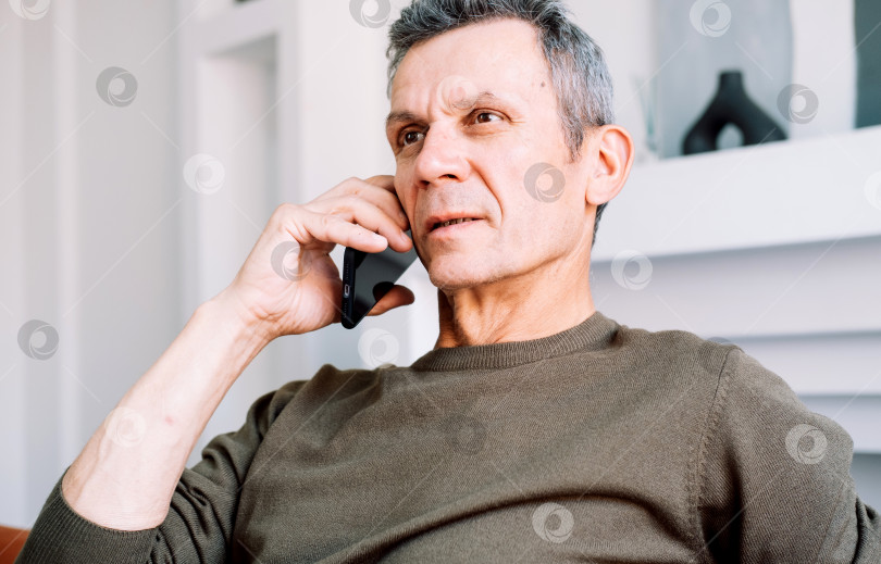 Скачать Серьезный озабоченный старик разговаривает по мобильному телефону, вызывая скорую помощь. фотосток Ozero