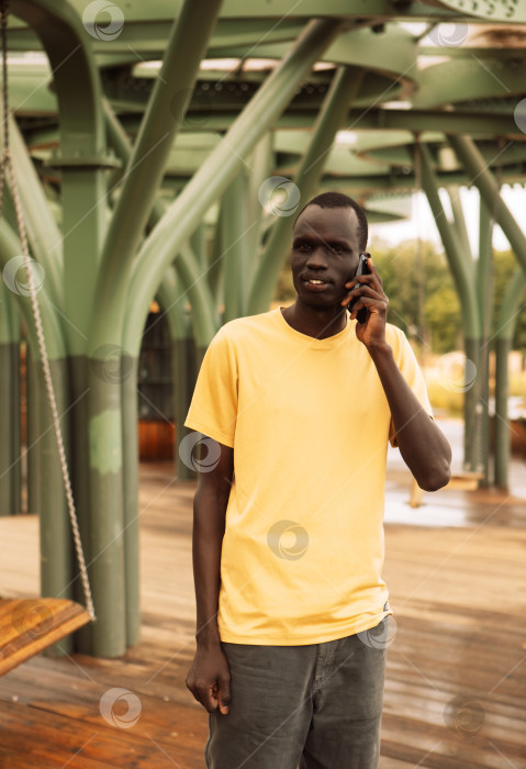 Скачать Серьезный чернокожий мужчина звонит по смартфону, стоя в парке фотосток Ozero