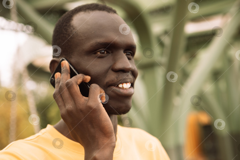 Скачать Серьезный чернокожий мужчина звонит по смартфону, стоя в парке фотосток Ozero