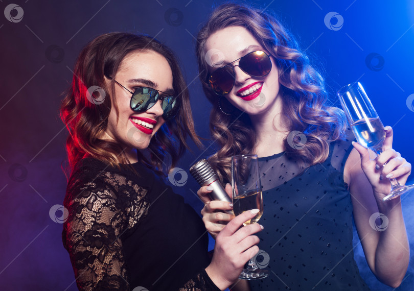 Скачать Две молодые симпатичные женщины в черном платье держат в руках бокал вина и поют в микрофон фотосток Ozero