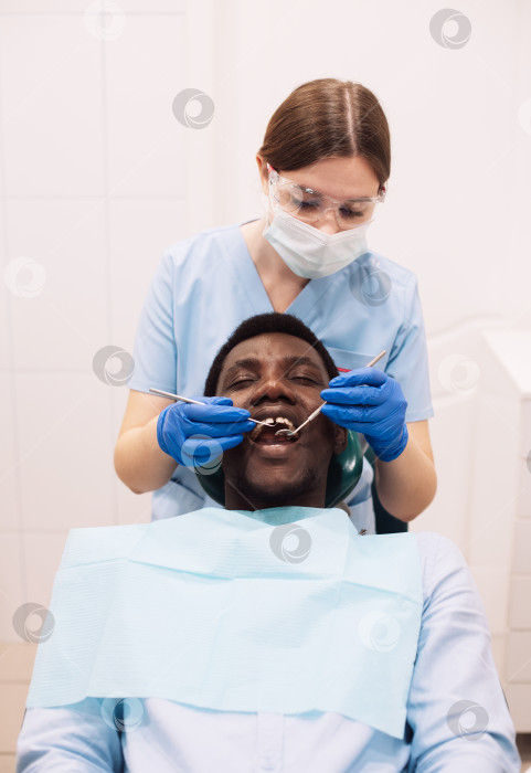 Скачать Портрет чернокожего пациента мужского пола, проходящего лечение зубов у стоматолога в современной клинике. фотосток Ozero
