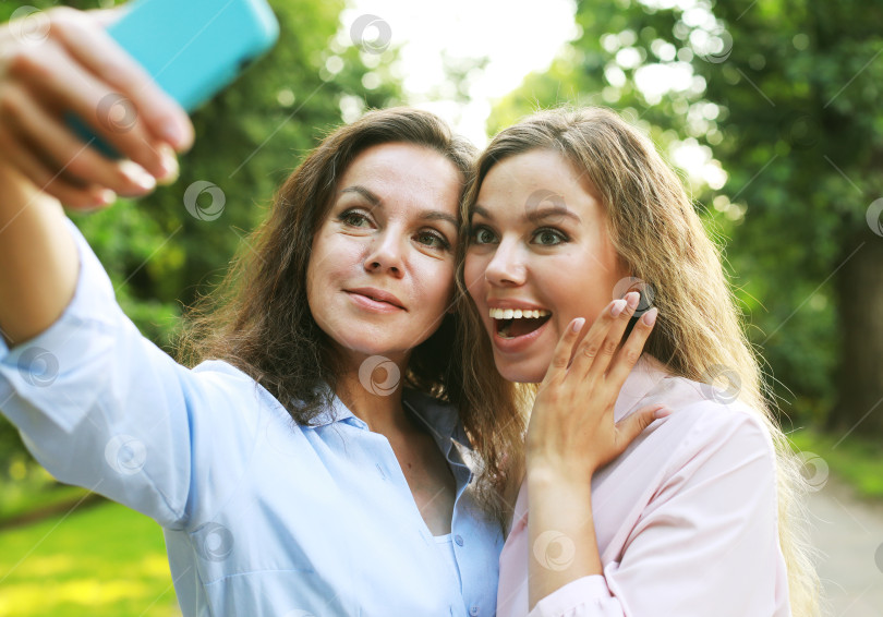 Скачать зрелая мать и взрослая дочь делают селфи на мобильный телефон в летнем парке фотосток Ozero