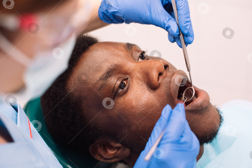 Скачать Портрет чернокожего пациента мужского пола, проходящего лечение зубов у стоматолога в современной клинике. фотосток Ozero