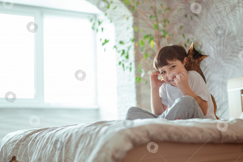 Скачать Маленький мальчик лежит в постели, расслабляясь со своим котенком. Счастливый ребенок с домашним животным, сидящим на кровати фотосток Ozero