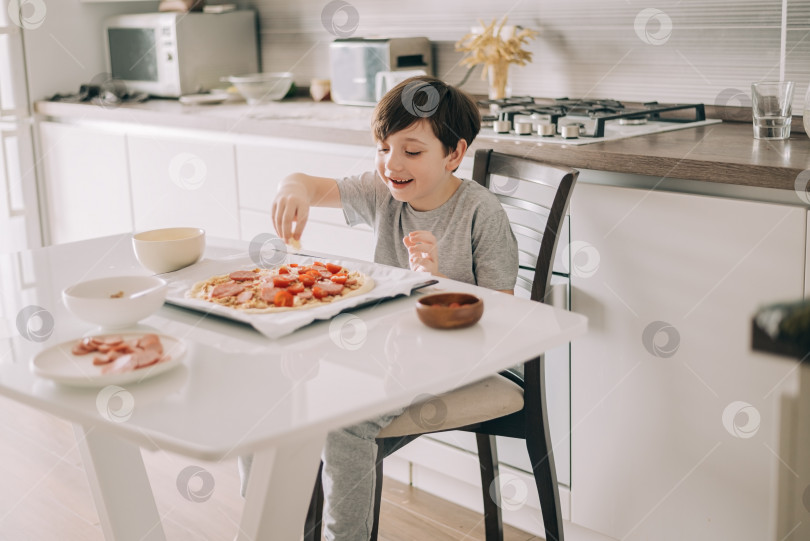 Скачать Маленький мальчик готовит пиццу, сидя за столом на кухне. Дети, помогающие в приготовлении пищи образ жизни фотосток Ozero