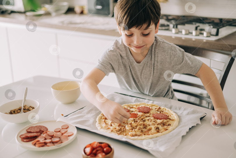 Скачать Маленький мальчик готовит пиццу, сидя за столом на кухне. Дети, помогающие в приготовлении пищи образ жизни фотосток Ozero