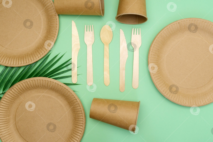 Скачать Бумажные стаканчики, тарелки и деревянные столовые приборы на зеленом фоне. Посуда из эко-крафтовой бумаги. Концепция "ноль отходов" и "экологичность". фотосток Ozero
