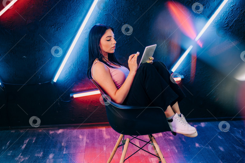 Скачать Используя планшет. Портрет кавказской женщины, выделенный на градиентном студийном фоне в неоновом свете. Красивая женская модель фотосток Ozero
