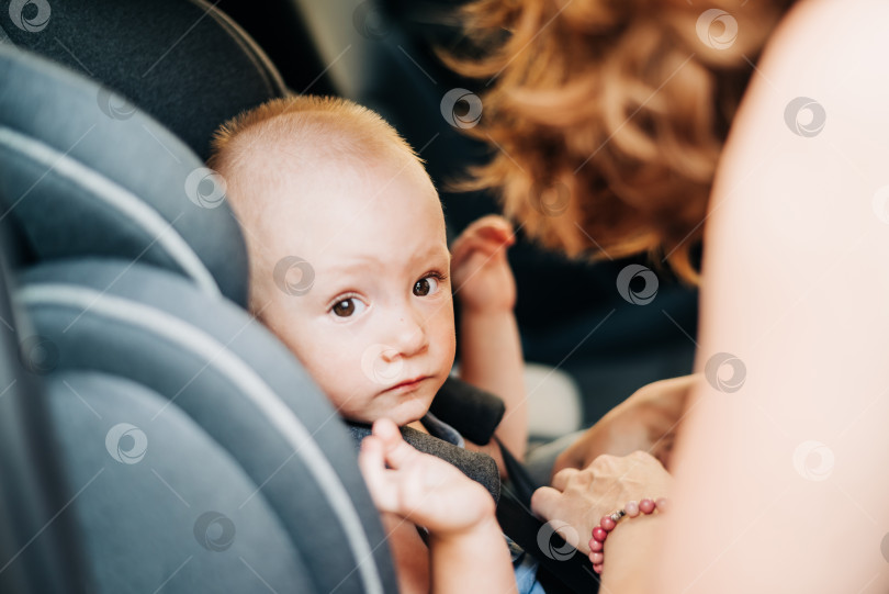 Скачать Маленькая девочка сидит в автокресле и смотрит в окно. Счастливый младенец с ремнем безопасности в автомобиле. Машина безопасности. фотосток Ozero