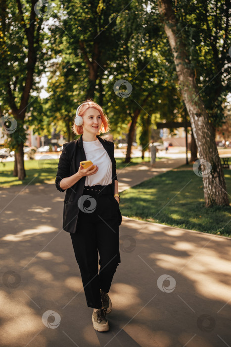 Скачать Молодая блондинка в наушниках и с мобильным телефоном в руках в парке на открытом воздухе в солнечный день фотосток Ozero