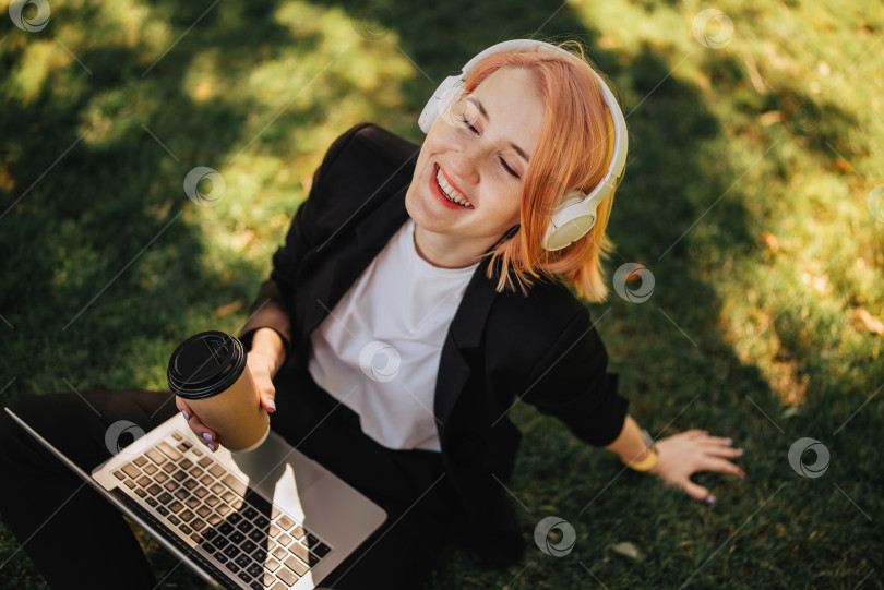 Скачать Симпатичная молодая кавказская женщина выходит на прогулку в парк с кофе и ноутбуком. Работа на открытом воздухе фотосток Ozero