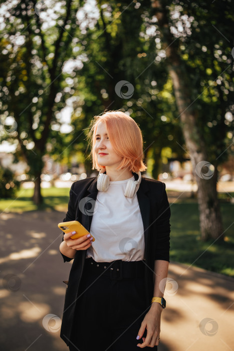 Скачать Молодая блондинка в наушниках и с мобильным телефоном в руках в парке на открытом воздухе в солнечный день фотосток Ozero