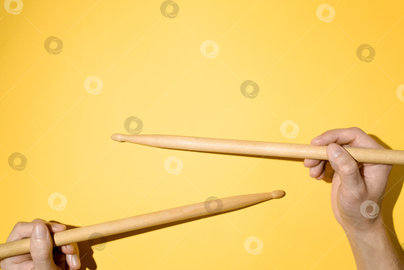 Скачать Мужские руки, держащие барабанные палочки, вид сверху на желтом фоне. Барабанщик фотосток Ozero