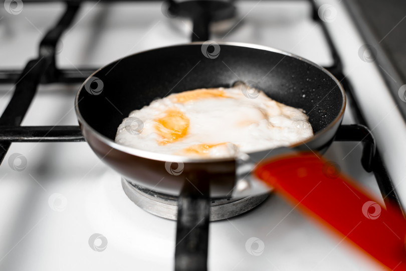 Скачать Яичница-глазунья на сковороде, крупным планом. Маленькая сковородка, стоящая на газовой плите, в помещении. Избирательный фокус. Концепция утреннего завтрака фотосток Ozero